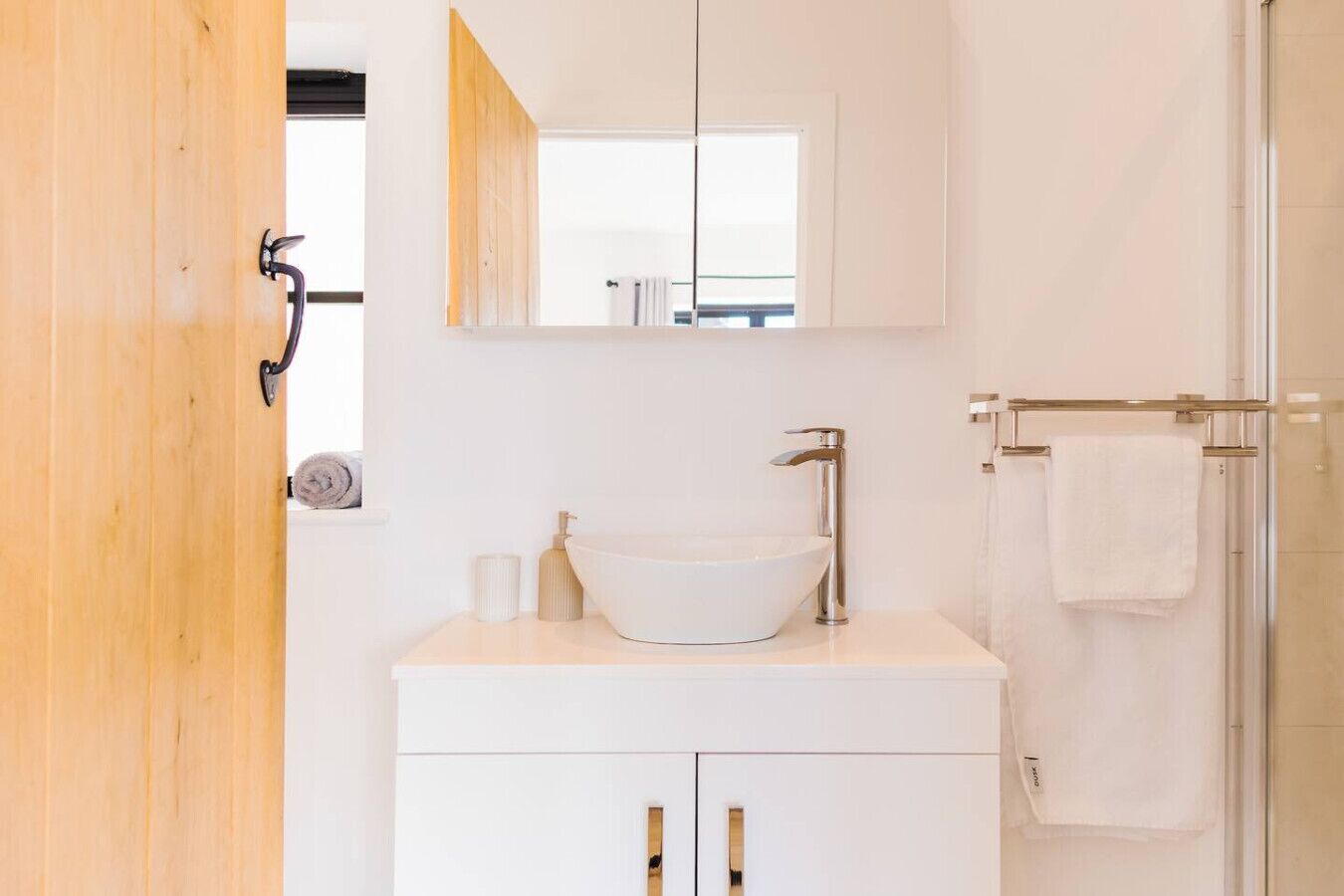 Un baño moderno con un lavamanos blanco, un espejo y un perchero para toallas.