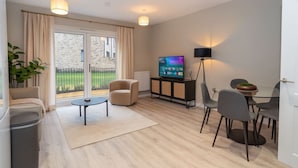 A modern living room with a sofa, armchair, TV, and dining area. - Belgrave Village Home: Patio, Parking & Gym (Balsall Heath)