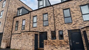A modern brick building with multiple windows and doors, featuring a flat roof and a small garden area in front. - Belgrave Village Home: Patio, Parking & Gym (Balsall Heath)