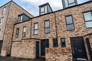 A modern brick building with multiple windows and doors, featuring a flat roof and a small garden area in front. - Belgrave Village Home: Patio, Parking & Gym (Balsall Heath)