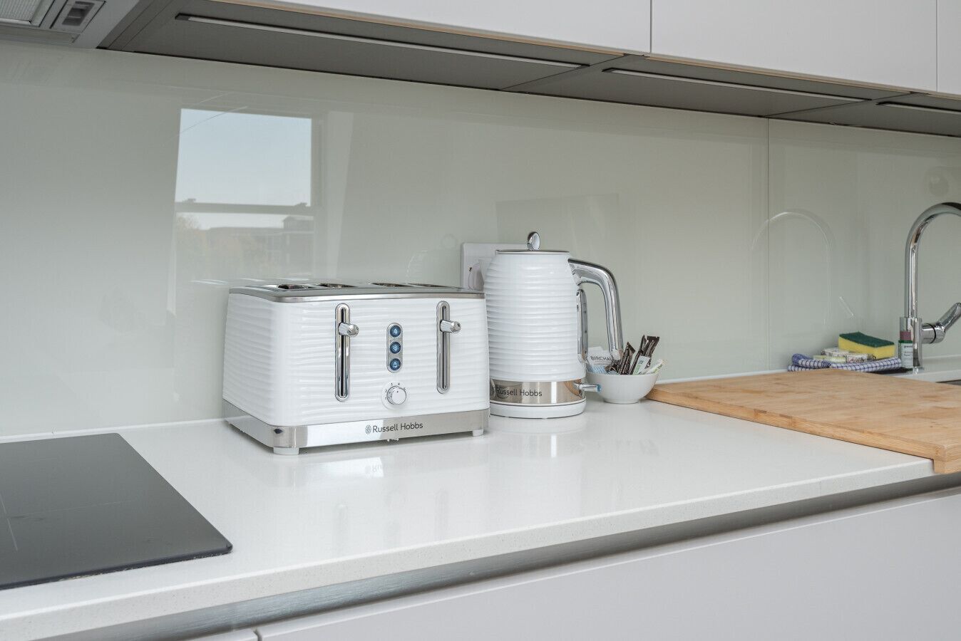 Una cocina con encimera blanca, tostadora, hervidor y cafetera.