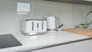 Une cuisine avec un plan de travail blanc, un grille-pain, une bouilloire et une machine à café.