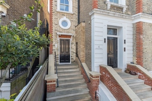 A narrow staircase leading to a door with a round window above it, flanked by brick walls and a small tree. - 1850s Victorian Villa with Garden Views, Fulham (Greater London)