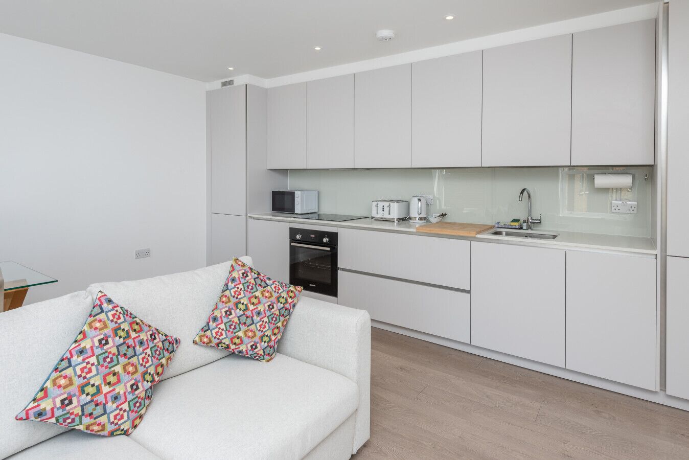 A modern kitchen with white cabinets, a microwave, a toaster, and a sink.