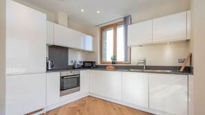 Een moderne keuken met witte kastjes, een roestvrijstalen oven, een magnetron en een raam met een plant op het aanrecht.