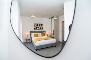 Ein Schlafzimmer mit einem Bett, Nachttischlampen, einem Spiegel und einem Wandbild.