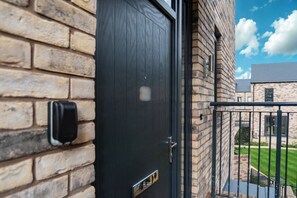 Eine schwarze Tür mit Briefkasten, eine Ziegelwand und ein Balkon mit Metallgitter.