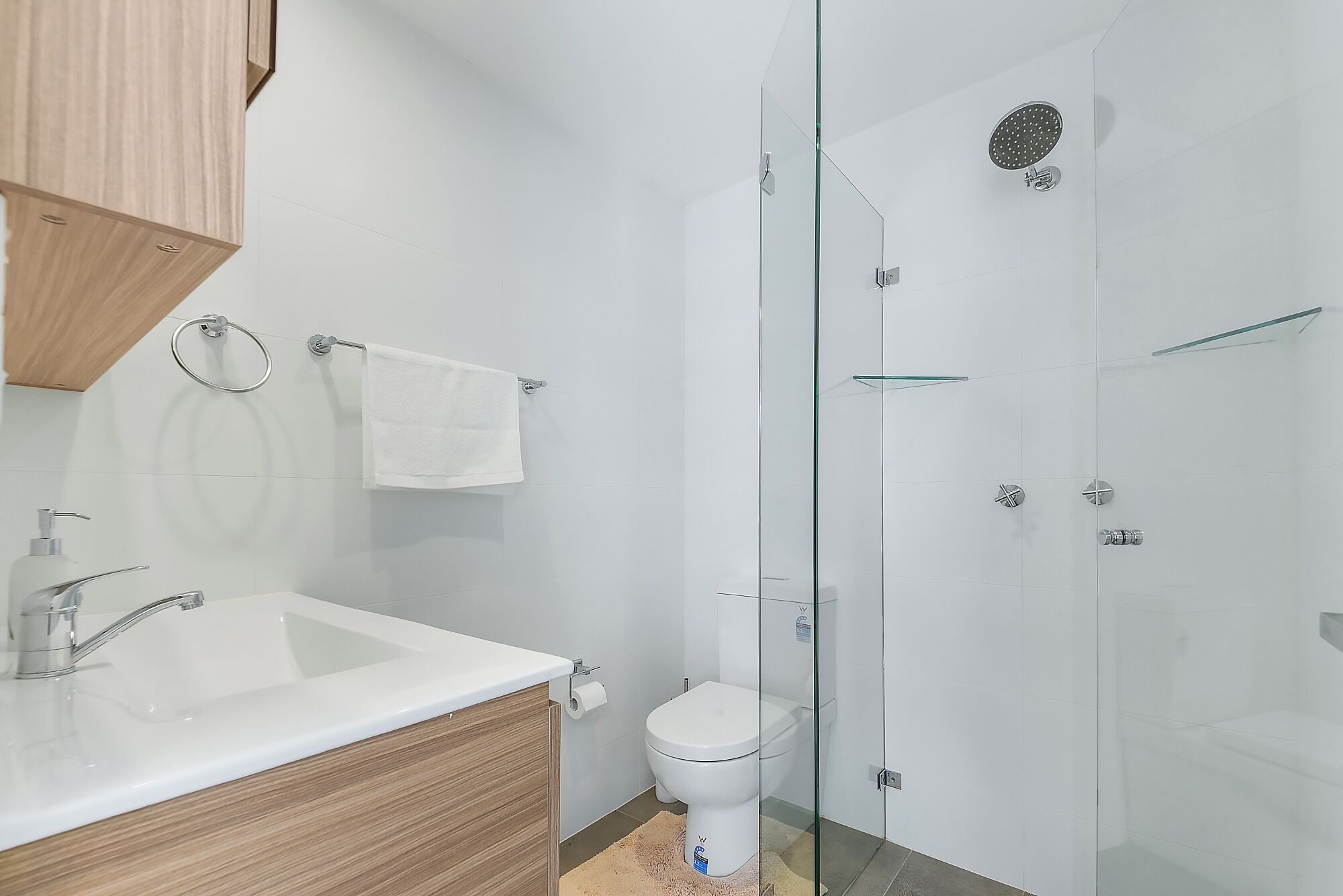 A modern bathroom with a glass shower enclosure, a white toilet, and a wooden vanity with a sink.