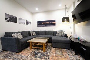Een moderne woonkamer met een modulaire bank, een salontafel, een gekleurd vloerkleed en kunstwerken aan de muur.