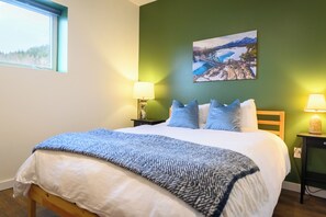 Ein ordentlich gemachtes Bett mit einer blau-weißen Decke, eine grüne Wand mit einem Gemälde und zwei Nachttischlampen.