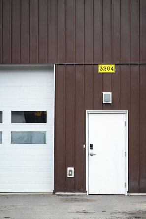 Een gebouw met een bruine gevel, een witte garage deur en een witte deur met daar boven een bord met het nummer 3204.