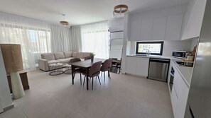 Eine moderne Küche mit weißen Schränken, ein Essbereich mit Tisch und Stühlen und ein Wohnbereich mit einer Couch und Vorhängen.