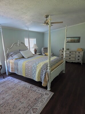 A four-poster bed with a canopy, a bedside table with a lamp, a chair, a dresser, and a rug.