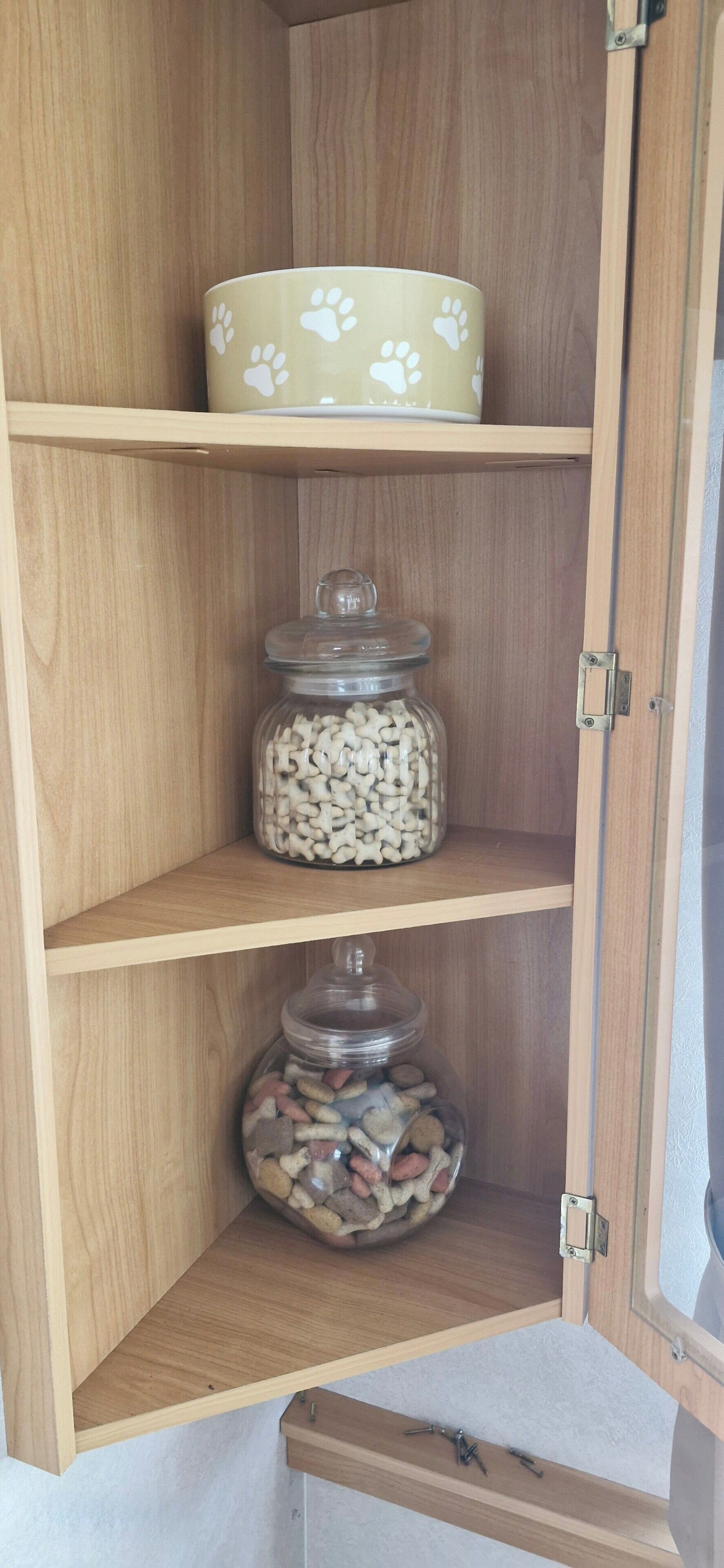 A wooden cabinet with three shelves, each containing a different item: a bowl, a jar of white objects, and a jar of mixed objects.