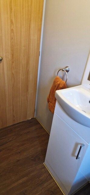 Une salle de bain avec une porte en bois, un meuble blanc avec un lavabo et une serviette suspendue à un porte-serviettes en métal.