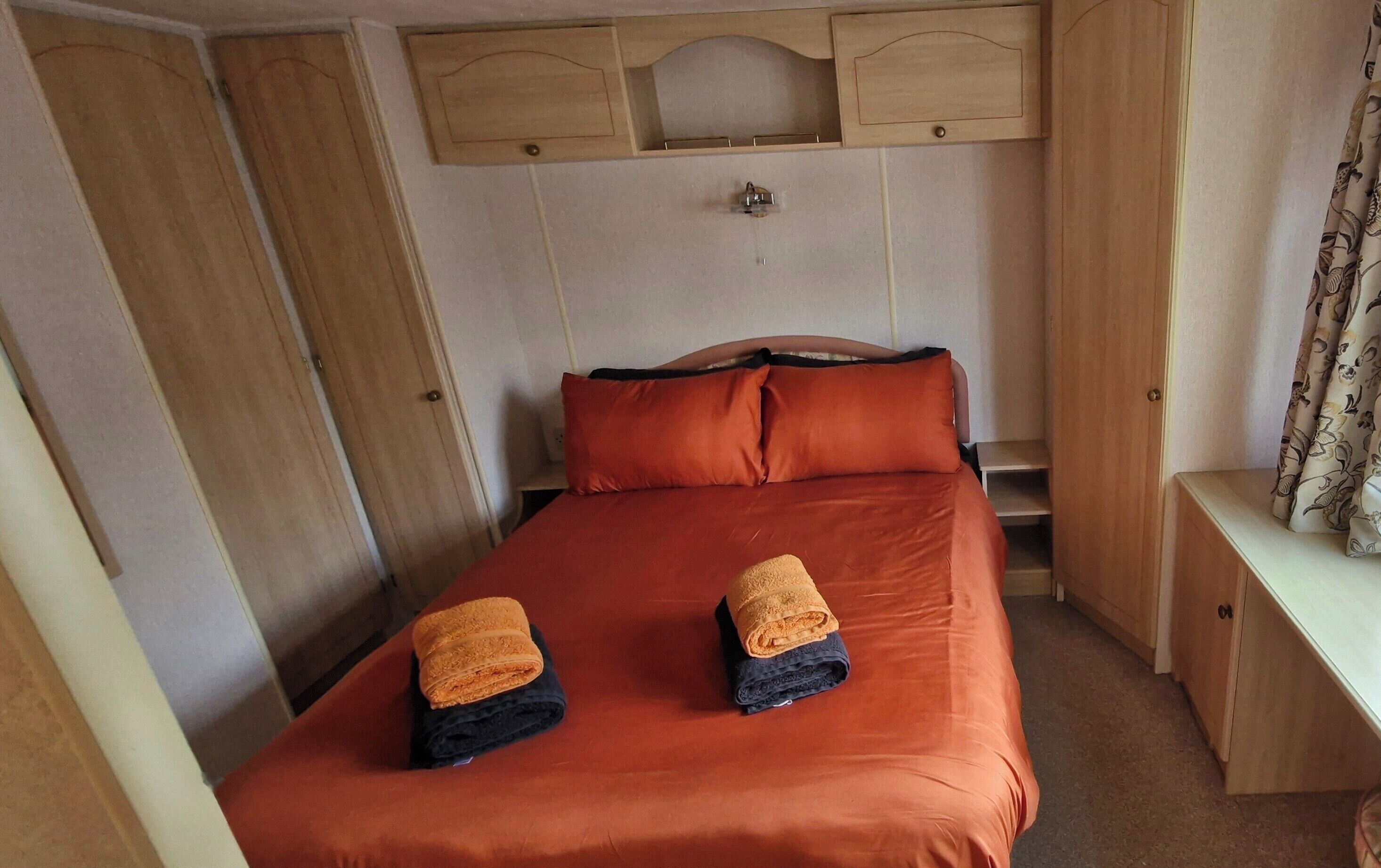 A bedroom with a bed, two pillows, a nightstand, a wardrobe, and a mirror.