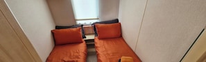 A narrow room with two beds, each with an orange pillow, a small table, and a window with a view. - Cabin Sleeps 4 With Parking (Forfar)
