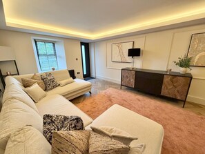 Ein modernes Wohnzimmer mit einer Eckcouch, einem Konsolentisch und einem großen abstrakten Gemälde an der Wand.