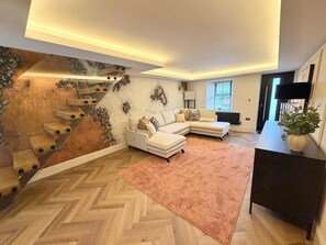 Ein modernes Wohnzimmer mit Fischgrätparkett, einem weißen Modulsofa, einer Treppe mit außergewöhnlichem Design und einer Topfpflanze.