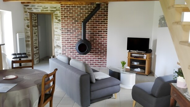 Un salon avec un mur en briques, un canapé, un téléviseur et un coin repas comprenant une table et des chaises.