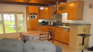 Une cuisine avec des meubles de rangement en bois, un four à micro-ondes, une cuisinière et un évier. On aperçoit une table à manger avec des chaises et un canapé au premier plan.