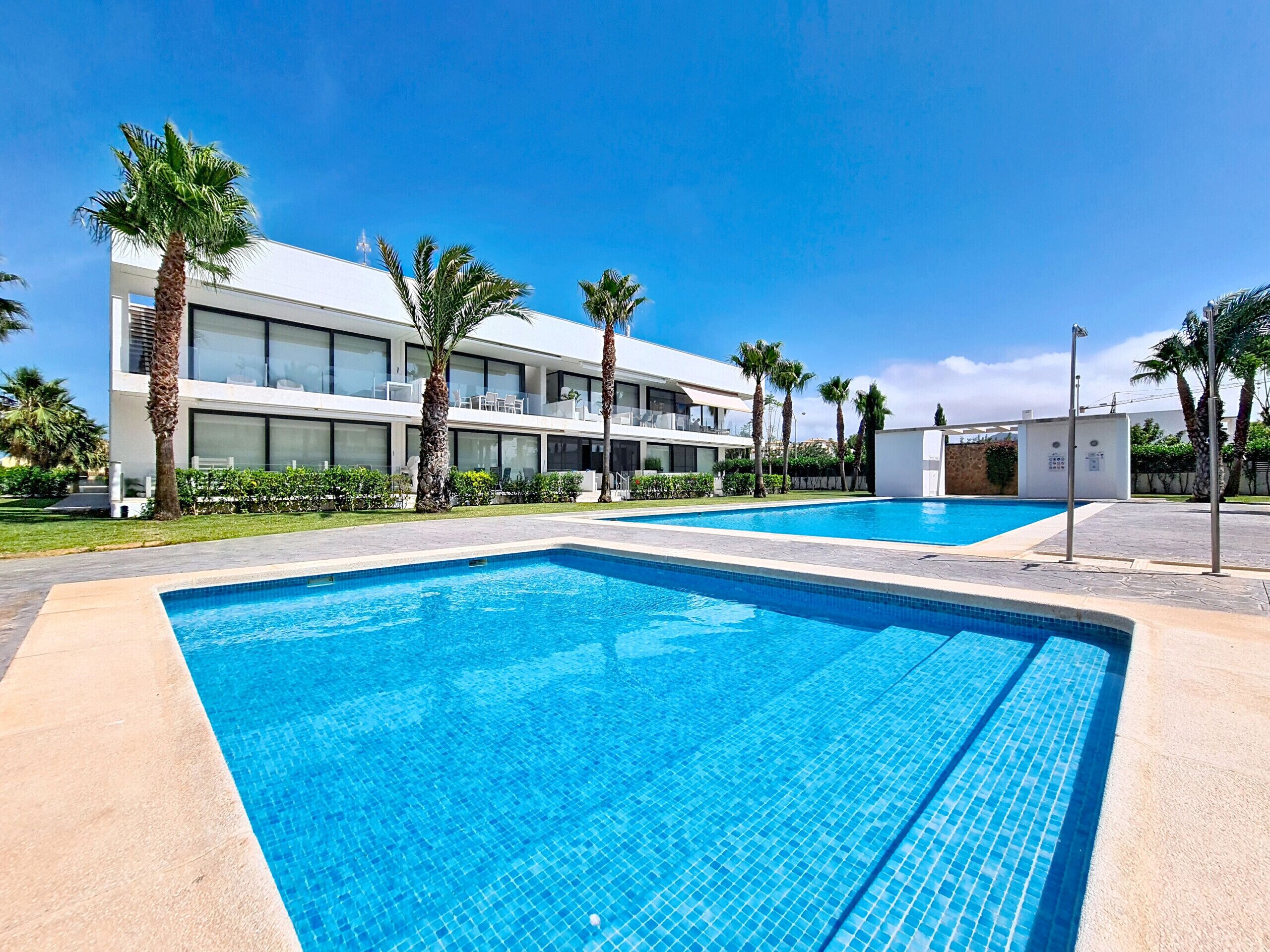 Un hôtel moderne doté d’une piscine, de palmiers et surplombant un ciel d’un bleu éclatant.