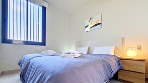 Een slaapkamer met een bed, twee nachtkastjes, een raam en een wandlamp.