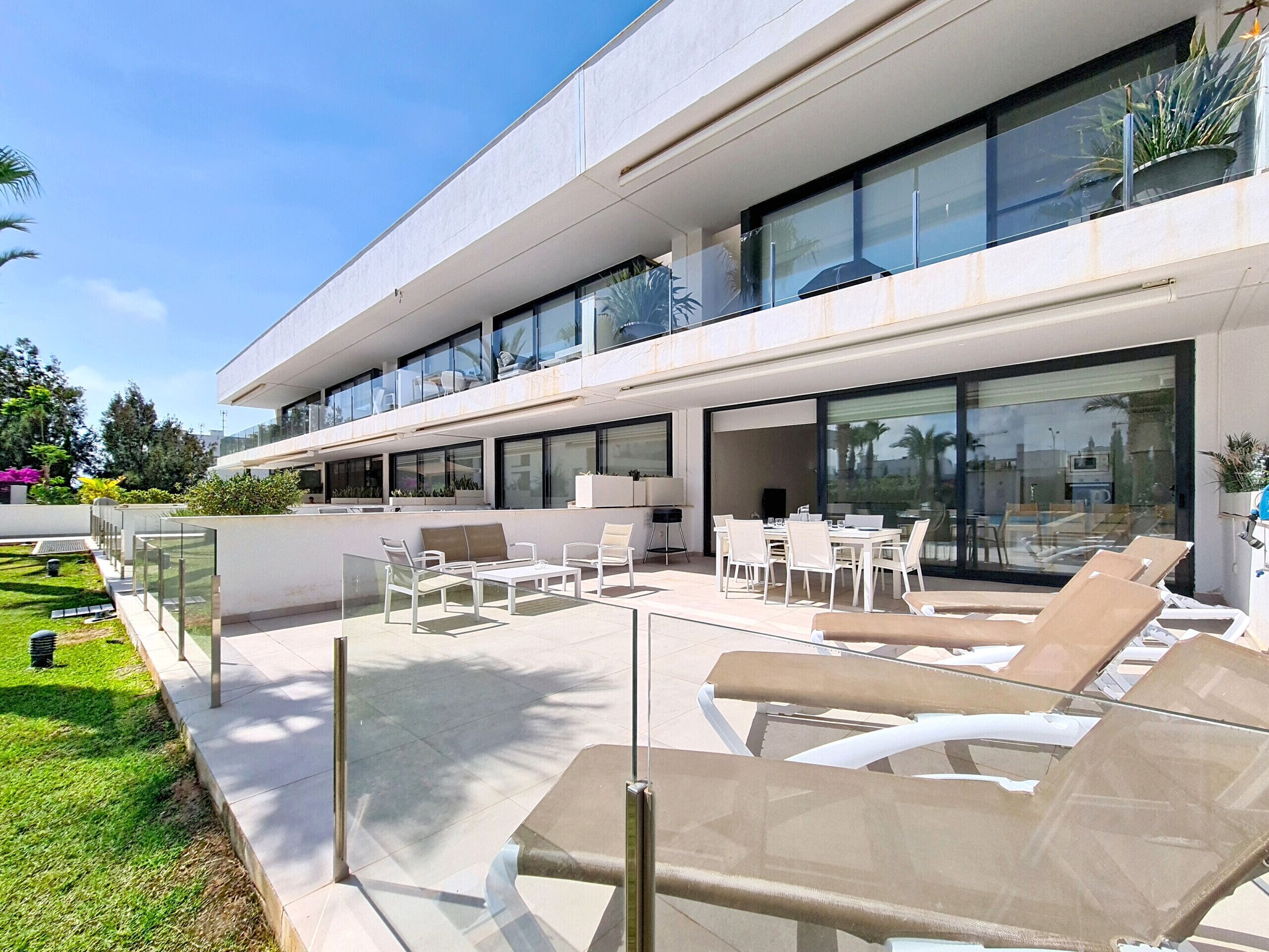 A modern building with a patio area featuring outdoor furniture and a glass railing.