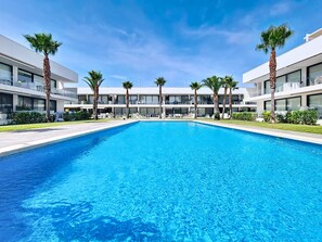A swimming pool with clear blue water, surrounded by modern buildings and palm trees. - Ground Floor Apartment with Direct Pool Access (Mar de Cristal)