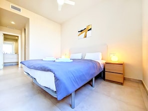 A modern hotel room with a large bed, bedside tables, a ceiling fan, and a bathroom visible through an open door. - Ground Floor Apartment with Direct Pool Access (Mar de Cristal)