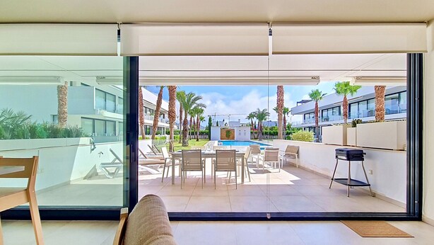 Een moderne hotelkamer met een glazen deur naar een zwembad, zitplaatsen buiten en uitzicht op de omliggende gebouwen.