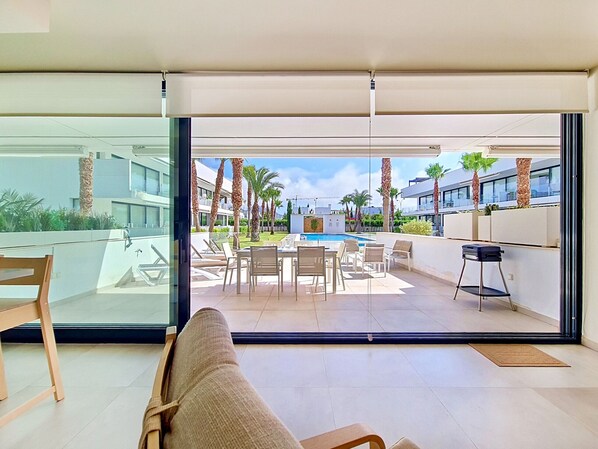 A modern hotel room with a glass door leading to a pool area, outdoor seating, and a view of the surrounding buildings. - Ground Floor Apartment with Direct Pool Access (Mar de Cristal)