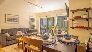 Un comedor con una mesa dispuesta para cuatro personas, un sofá y un televisor en la pared.
