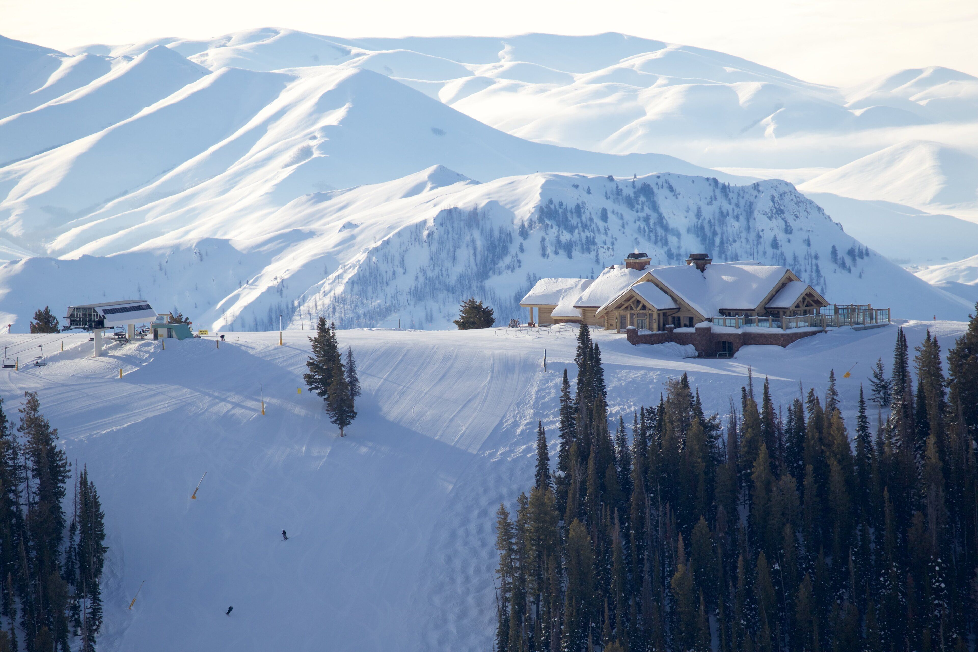 Une montagne enneigée, avec un chalet à l’extérieur en bois et un télésiège visible au loin.