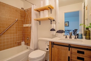 A bathroom with a bathtub, toilet, shower, wooden shelves, and a sink. - Stonehenge Condo #6 - Walk to River Run & Main Street (Ketchum)