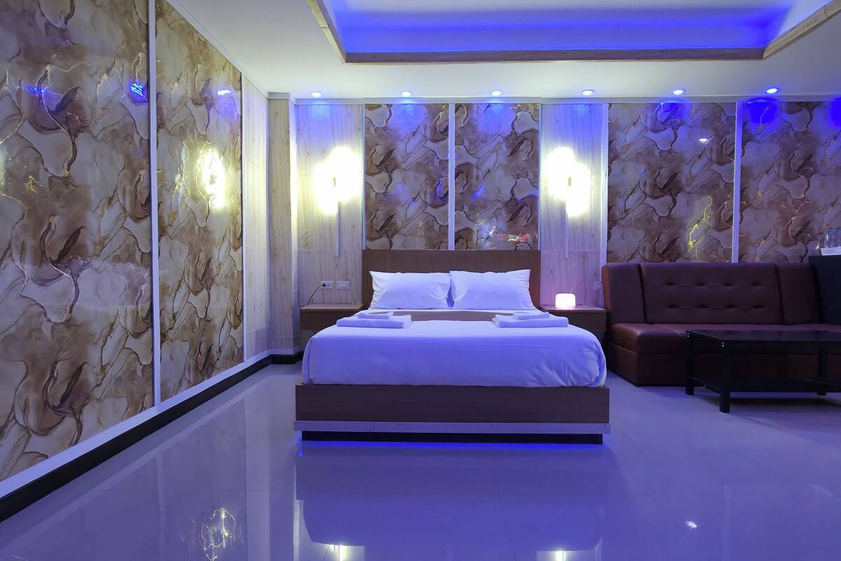 A modern hotel room with a large bed, a seating area, and a view of the city.