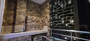 Un baño con pared de piedra, una bañera y un balcón con barandilla.