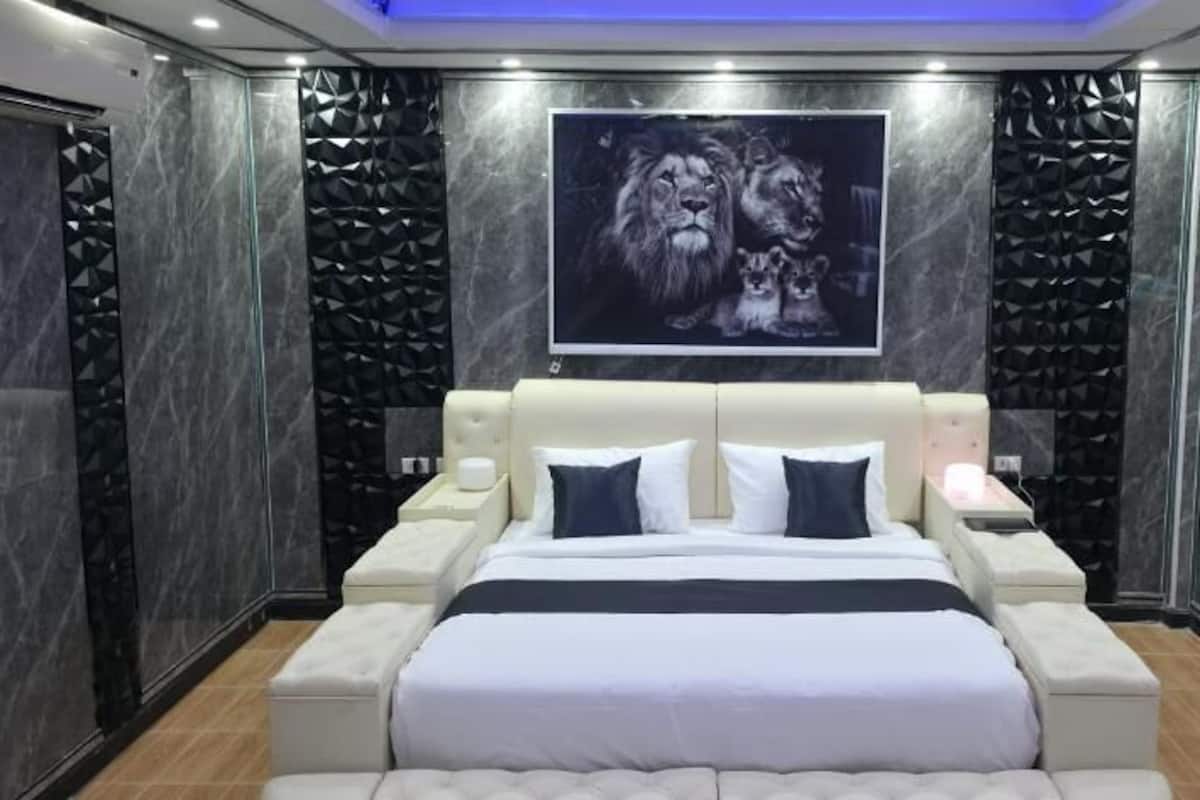 A modern bedroom with a large bed, a headboard, bedside tables, and a wall-mounted artwork.