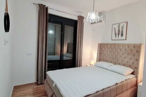 Ein Schlafzimmer mit Bett, Vorhängen, einem Fenster, einer Wandklimaanlage und einer Deckenleuchte.