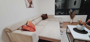 Ein modernes Wohnzimmer mit einem beigefarbenen Ecksofa, einem kleinen weißen Tisch und einer Vase mit Trockenblumen.