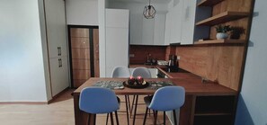 Eine moderne Küche mit weißen Schränken, einem Holztisch, zwei blauen Stühlen und einer Hängelampe.