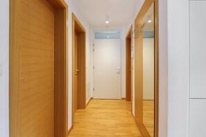 Un pasillo con puertas de madera, una puerta blanca al final y un artefacto de iluminación en el techo.