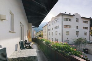 Een balkon met buitenmeubilair en uitzicht op omliggende gebouwen, met een berg op de achtergrond.