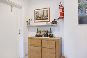 Een houten kast met decoratieve objecten, een lijst met schilderij, een aan de muur bevestigd brandblusapparaat, en een klein plankje met een klok.