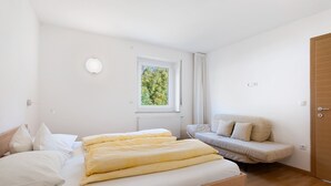 Un dormitorio con una cama de madera, una ventana con vistas a árboles, un sofá y una puerta.
