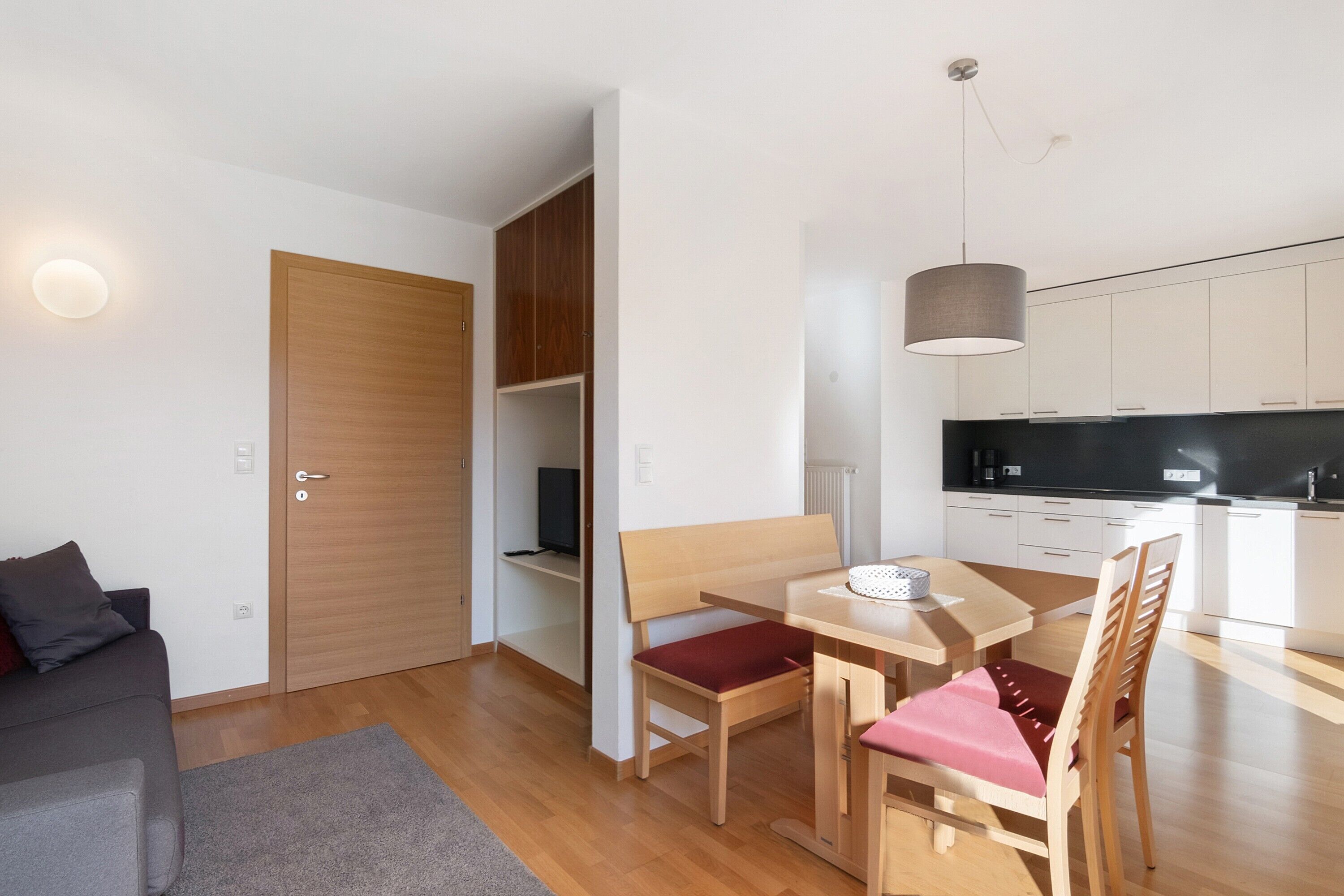 A modern living room with a sofa, a dining table with chairs, a kitchen area, and a wooden wardrobe.