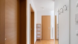 Un pasillo con piso de madera, una puerta de madera, una pared blanca con interruptor de luz y un perchero de metal.