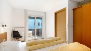 Habitación de hotel con cama, una silla, armario de madera y puerta corrediza de vidrio al balcón.