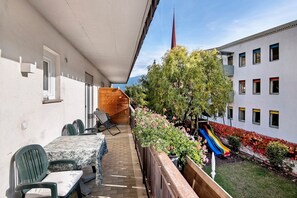 Ein Balkon mit Tisch und Stühlen, eine Rutsche und im Hintergrund ein Gebäude mit einem Turm.