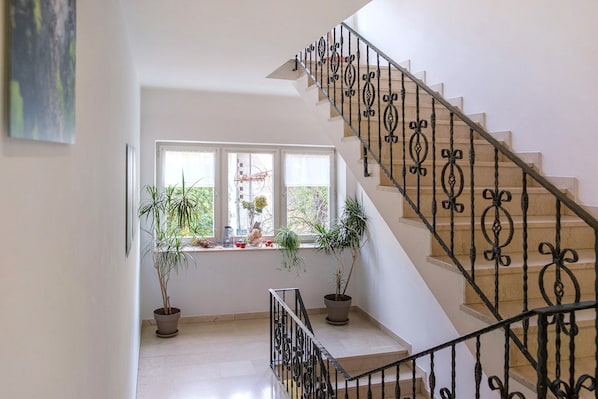Una escalera con barandillas negras decorativas, una ventana con plantas en macetas y vistas al verdor exterior.